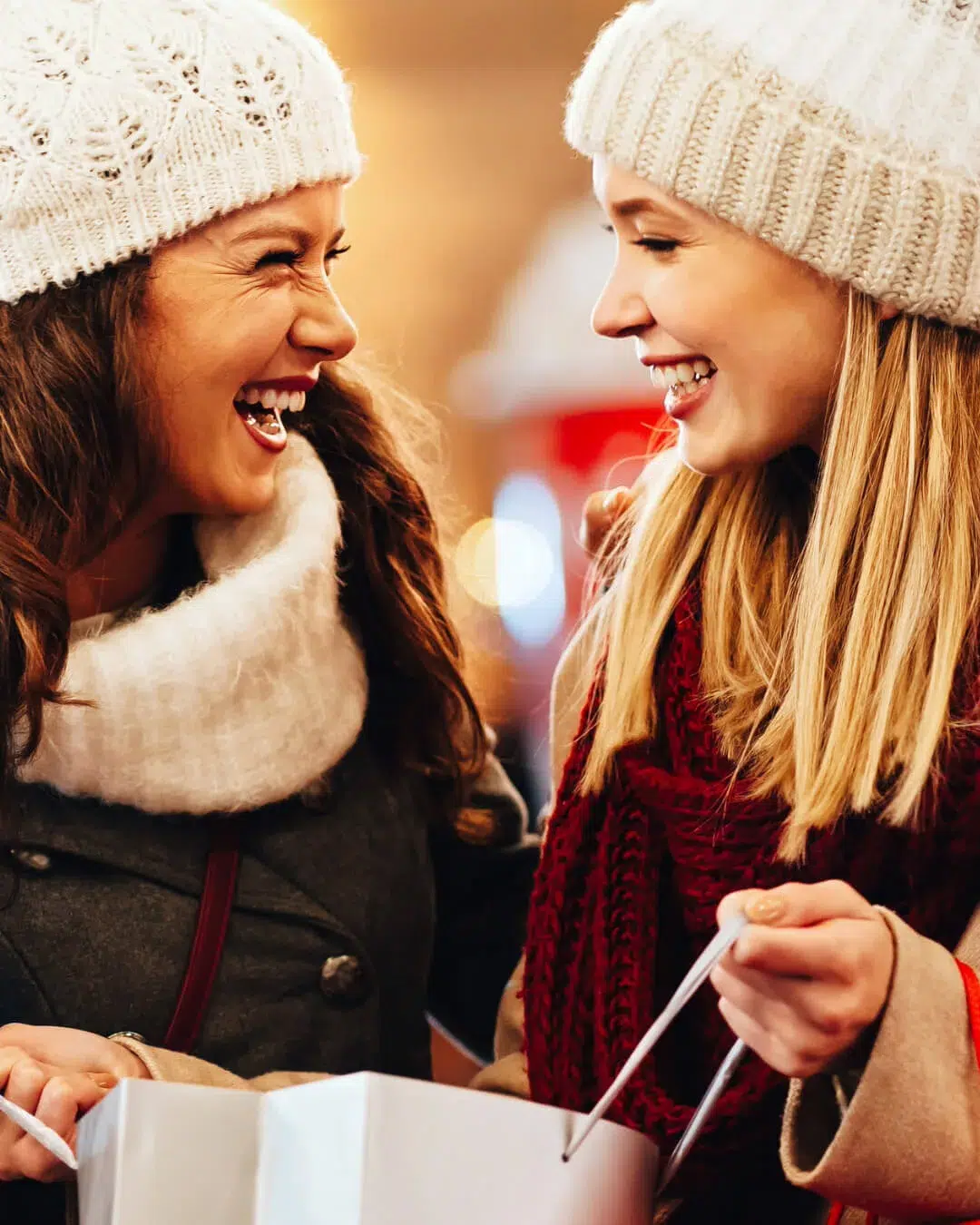 girls in wooly hats laughing together and holding christmas shopping bags